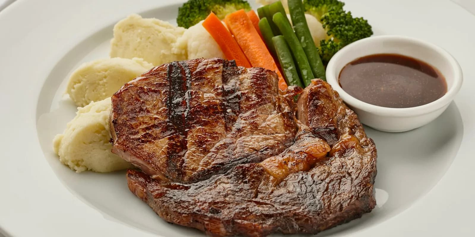 A white plate with seared beef and vegetables