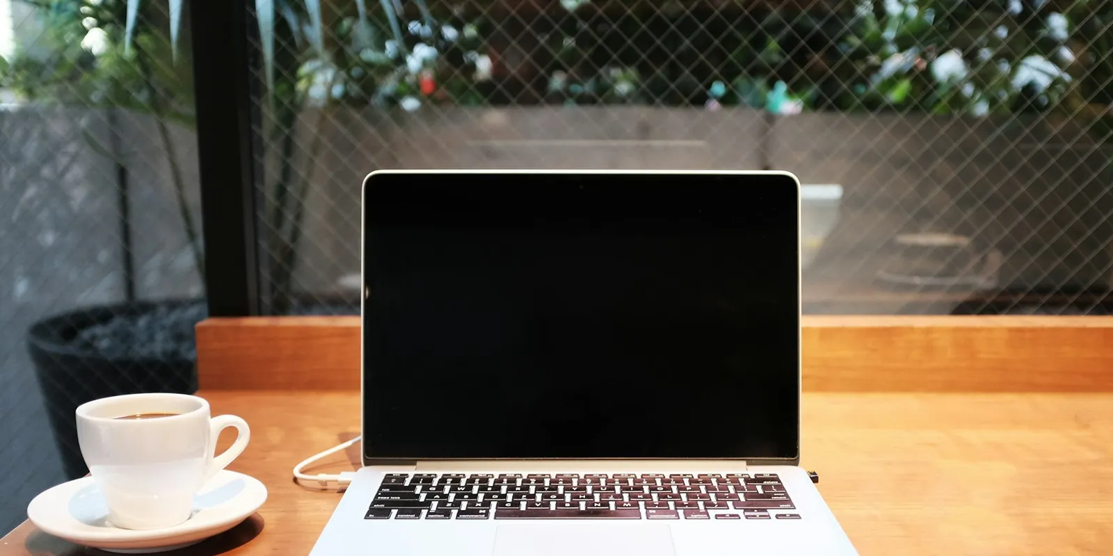 A laptop on a wooden desk beside a mug of coffee